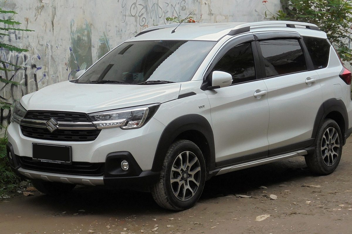 A white 2020 Suzuki XL7, the later Indonesian-market model, with black wheel-arch trim, parked on dirt beside a graffiti wall