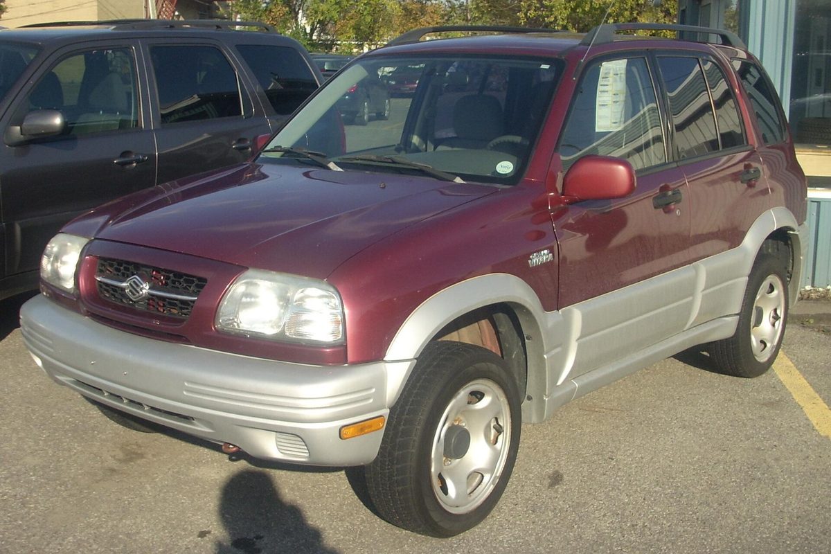 A dark red first-generation Suzuki Grand Vitara four-door with silver lower body trim, parked in a lot in Vaudreuil-Dorion, Quebec
