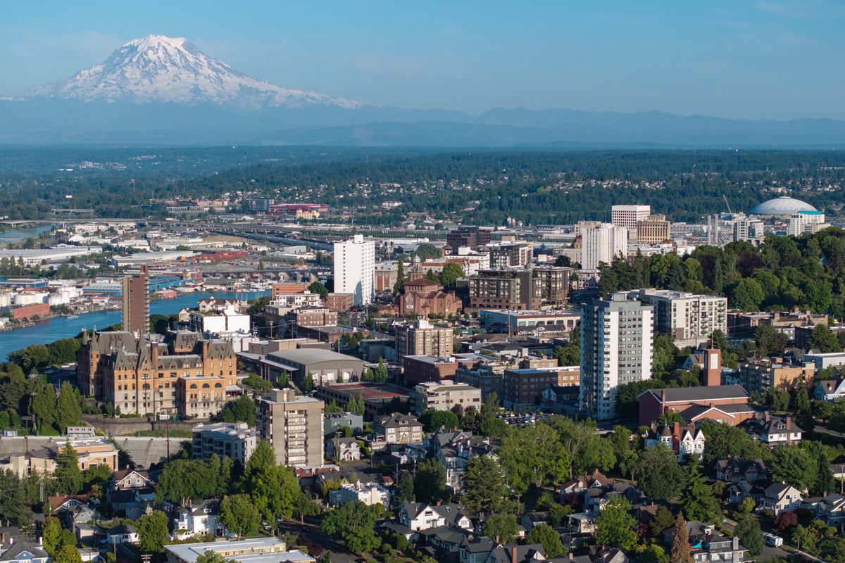 Tacoma's downtown and hillside neighborhoods from the air, with the waterway at left, a white domed arena at right and Mount Rainier behind
