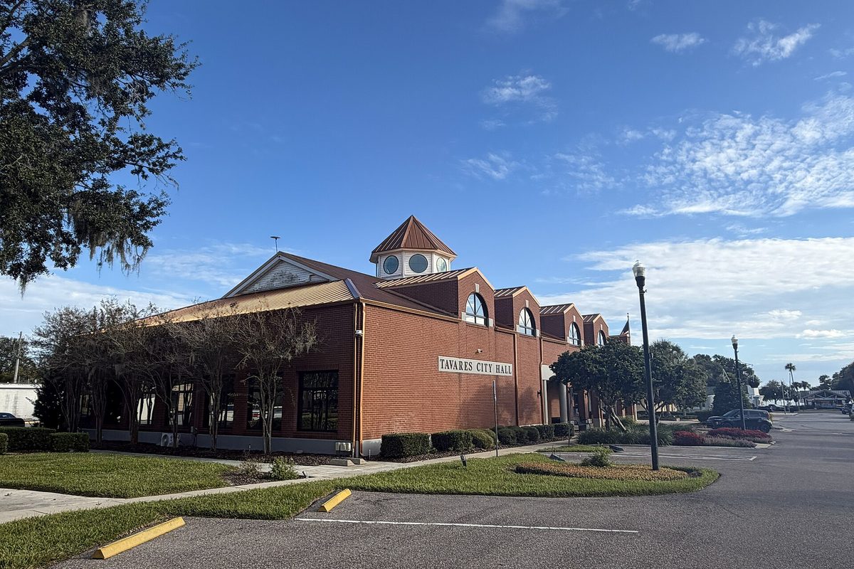 Tavares City Hall, a red brick building with arched upper windows and a small octagonal cupola, beside a parking lot under a blue sky