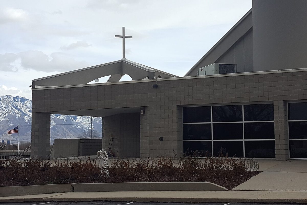 Saint Martin de Porres Catholic Church in Taylorsville, a gray block building with a pointed entry canopy topped by a cross, snowy mountains behind
