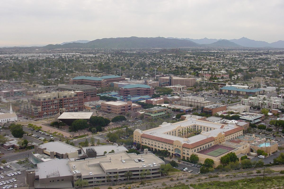 Downtown Tempe seen from above, with red-roofed mid-rise buildings, parking lots and a ridge of mountains under a gray sky
