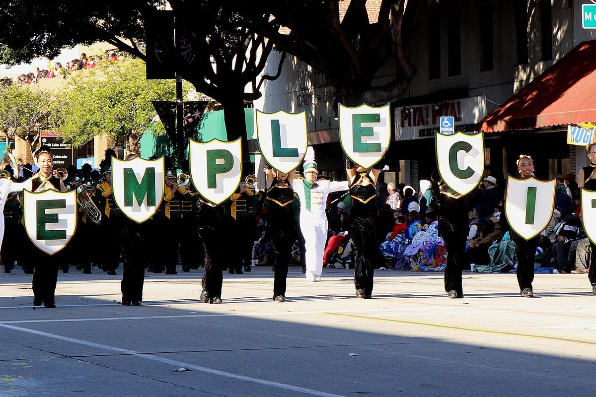Temple City High School marching band members in black and white carrying green-lettered shields down a parade street during the 2015 Rose Parade in Pasadena