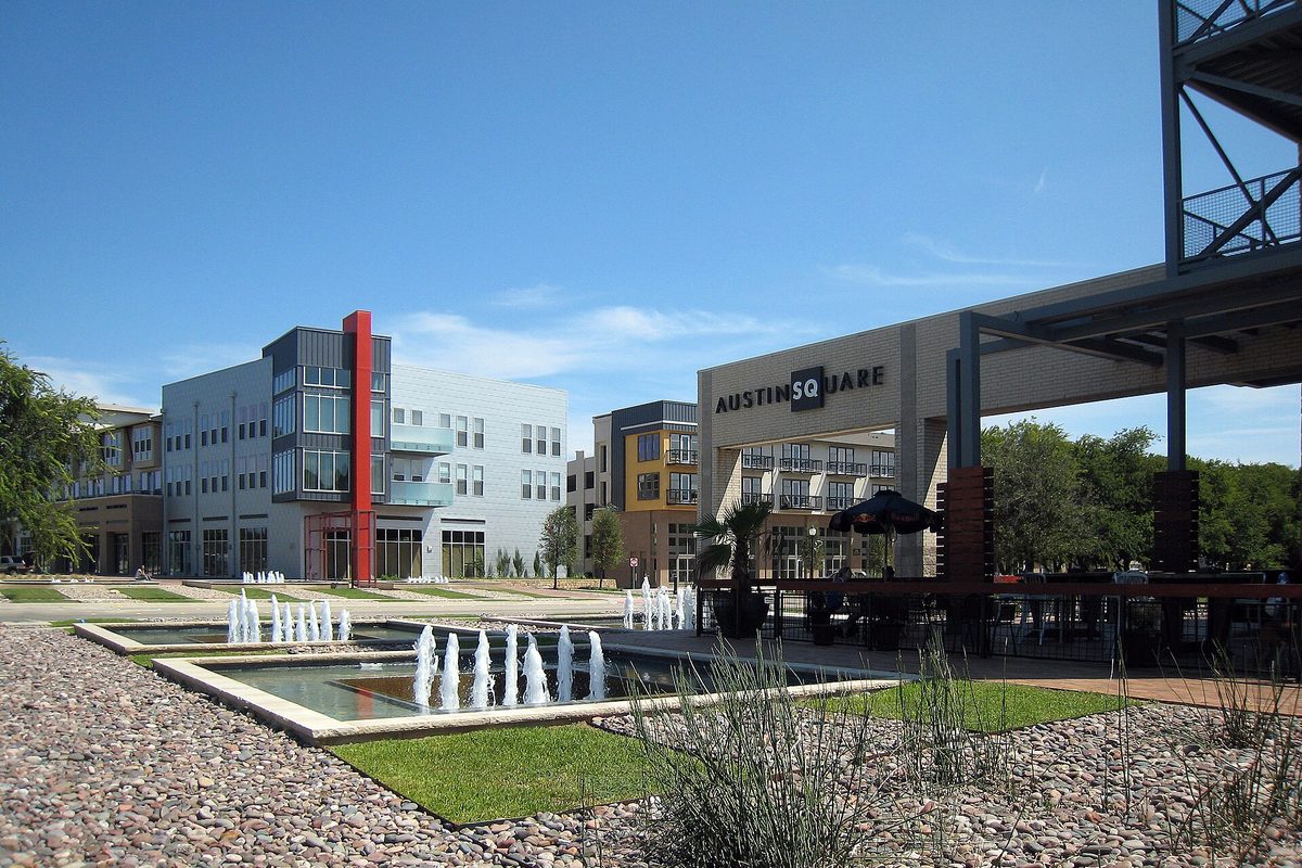 Austin Ranch's square in The Colony, with low fountains in a shallow pool, a gravel bed, the Austin Square sign and mid-rise apartment buildings