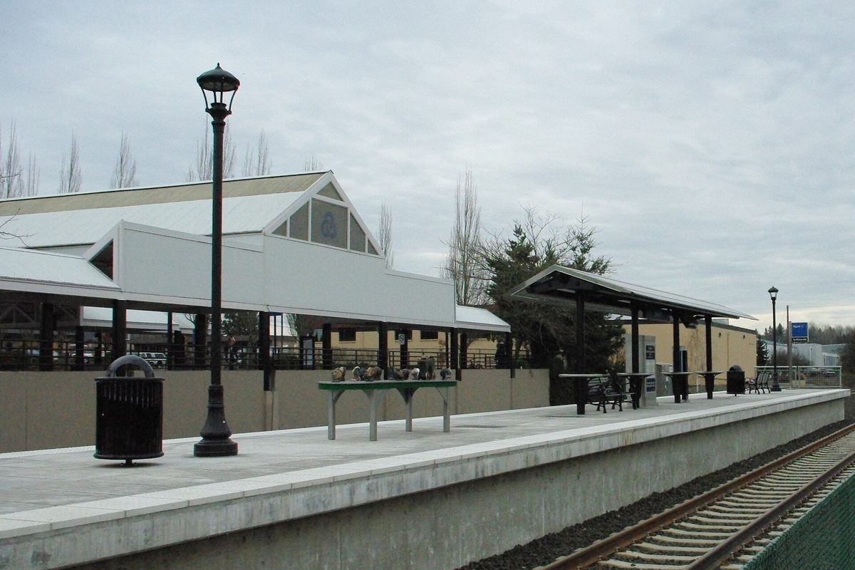 The Tigard Transit Center commuter rail platform, with covered shelters, a black lamp post and the tracks beside it under an overcast sky