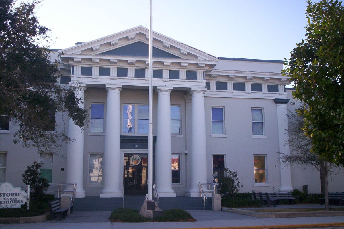 The historic Brevard County Courthouse in Titusville, a pale building with tall white columns and a triangular pediment, seen from the street