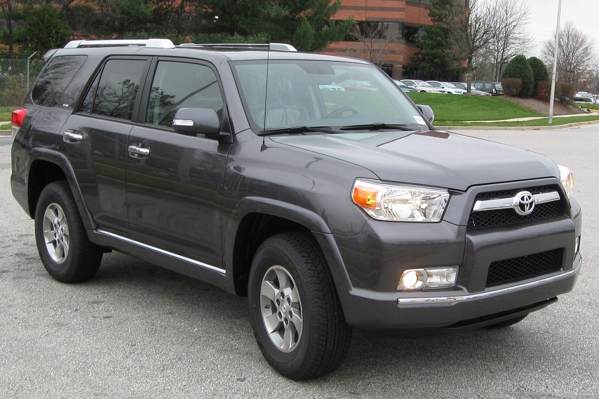 A dark gray 2010 Toyota 4Runner SR5 with silver alloy wheels and roof rails, parked in an office lot on a cloudy day