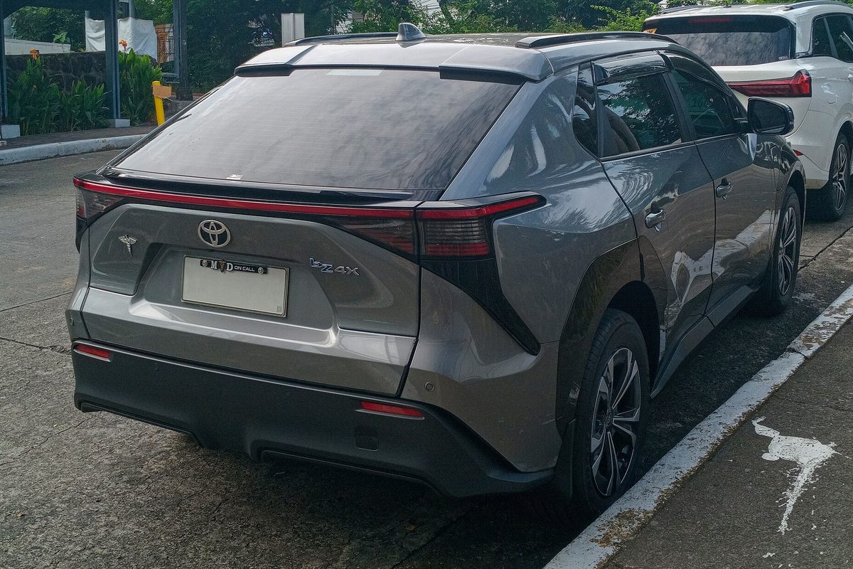 Rear view of a gray Toyota bZ4X parked at a curb, with a full-width red taillight bar across its hatch