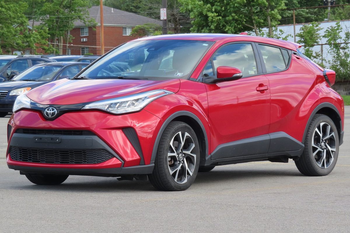 A red 2021 Toyota C-HR XLE with two-tone alloy wheels in a parking lot, with a brick building and trees behind it