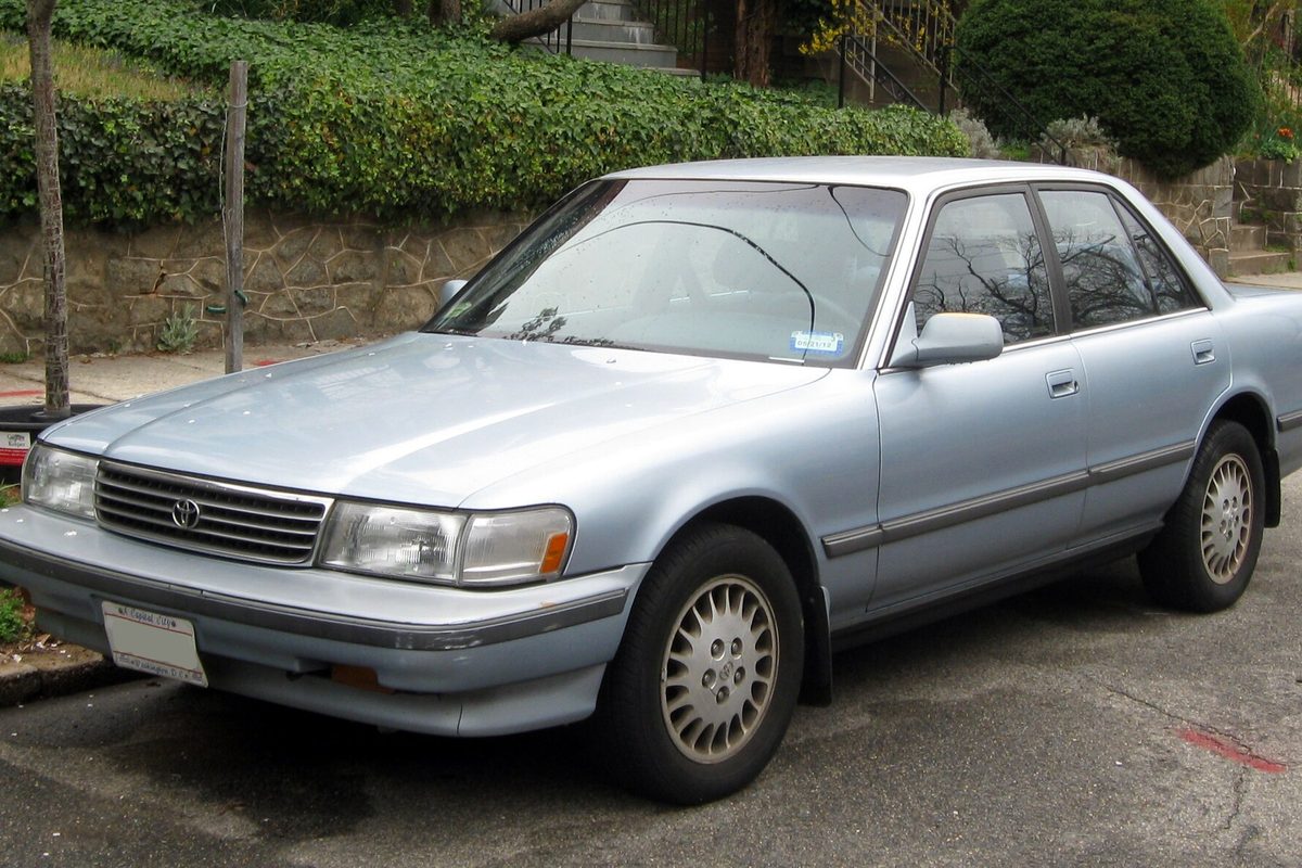 A pale blue 1991-1992 Toyota Cressida sedan parked at a curb in front of a stone wall covered in ivy