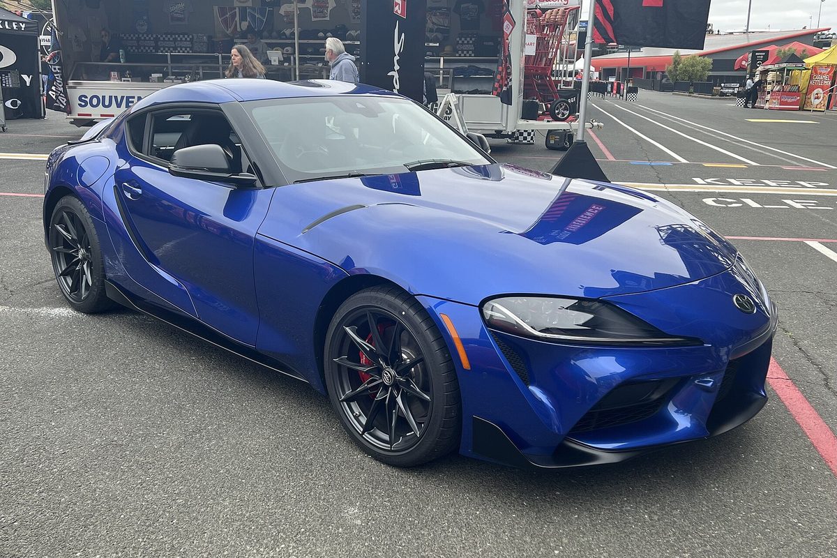 A blue Toyota GR Supra coupe with black wheels parked on the paddock pavement at Sonoma Raceway
