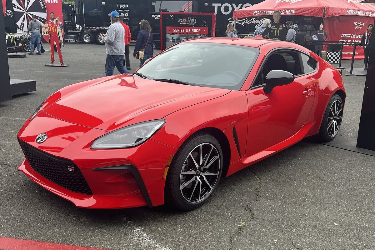 A red Toyota GR86 coupe on display at Sonoma Raceway in 2023, with a Toyota racing tent and visitors behind it