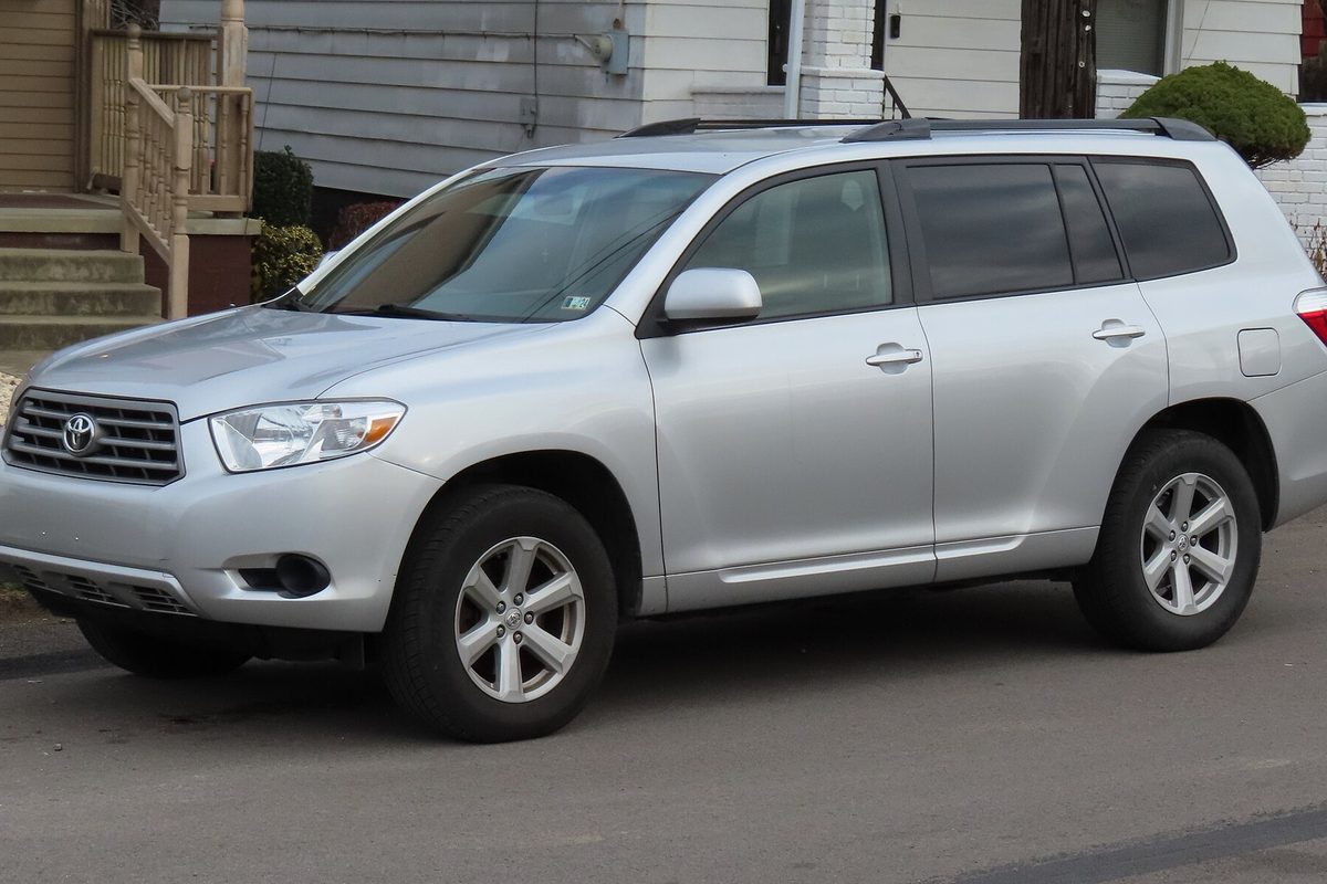 A silver 2009 Toyota Highlander parked at the curb of a residential street, with wooden porch steps behind it