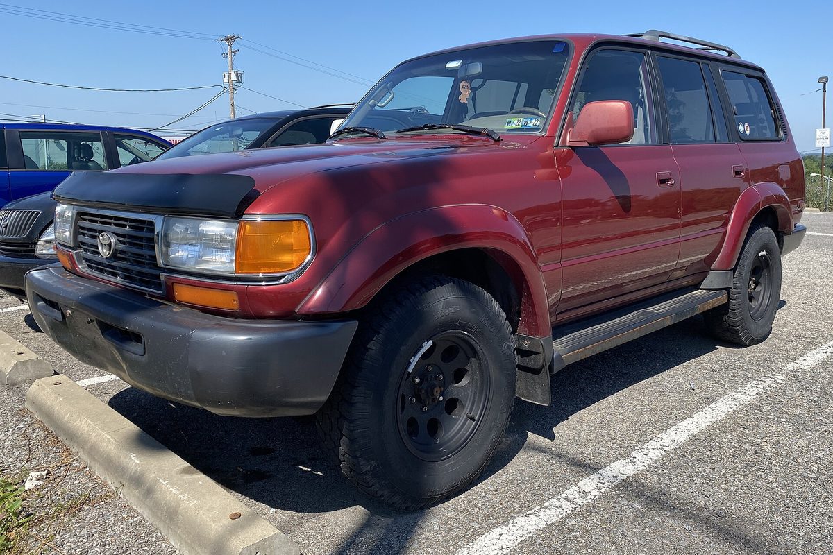 A dark red 1996 Toyota Land Cruiser with a black hood deflector and black steel wheels, parked in a lot