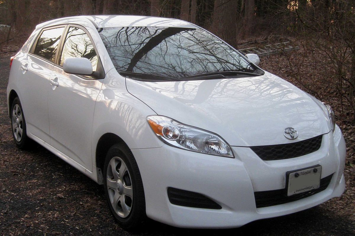 A white 2009 Toyota Matrix hatchback parked on a gravel drive, with bare winter woods behind it