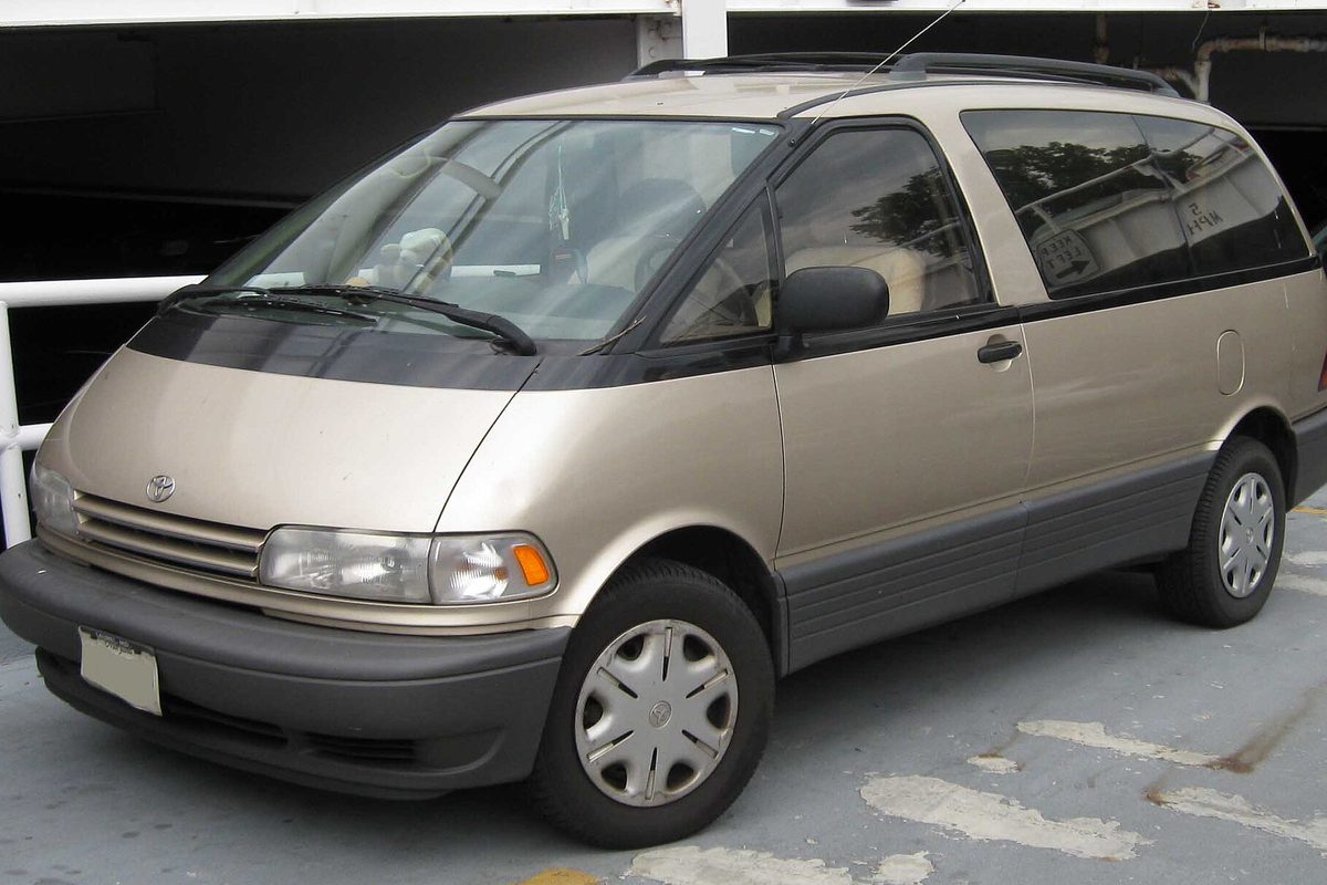A champagne first-generation Toyota Previa minivan with gray lower trim and plastic wheel covers, parked on a concrete garage deck