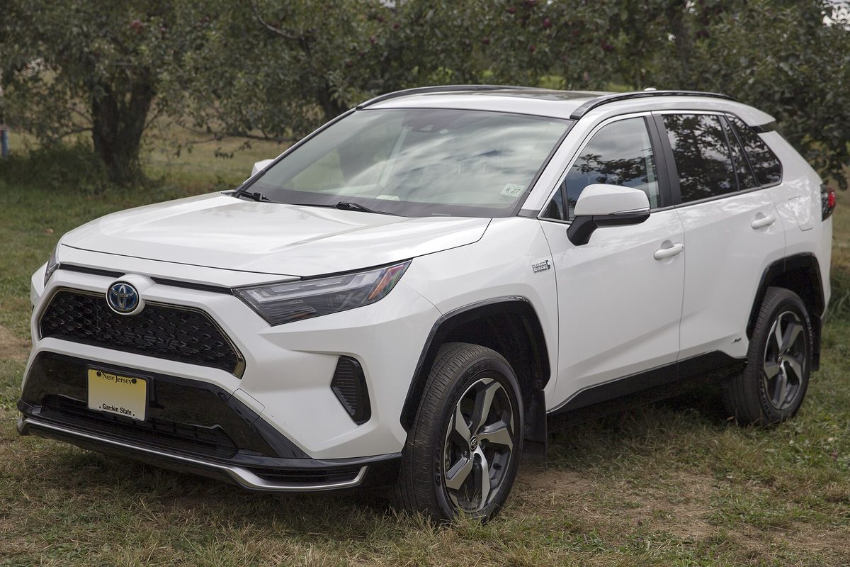 A white 2022 Toyota RAV4 Prime SE with black-trimmed bumpers parked on grass in front of apple trees
