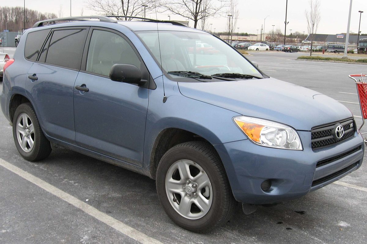 A blue 2006-2007 Toyota RAV4 parked in a store lot on a gray winter day, with a red shopping cart at the edge of the frame