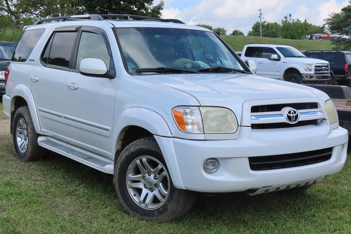 A white 2006 Toyota Sequoia Limited with roof rails and running boards, parked on grass in front of pickup trucks