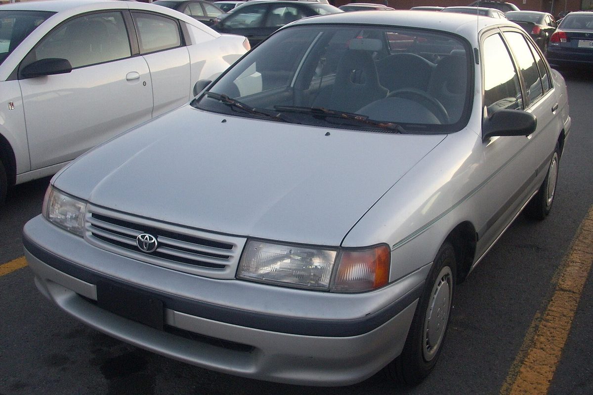A silver 1991 Toyota Tercel four-door sedan in a parking lot, with other cars parked close on both sides