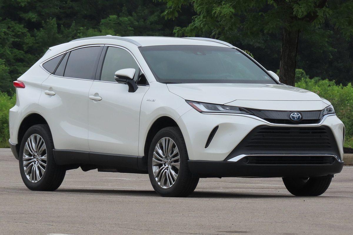 A pearl white 2021 Toyota Venza XLE hybrid crossover parked on an empty lot in front of a line of green trees