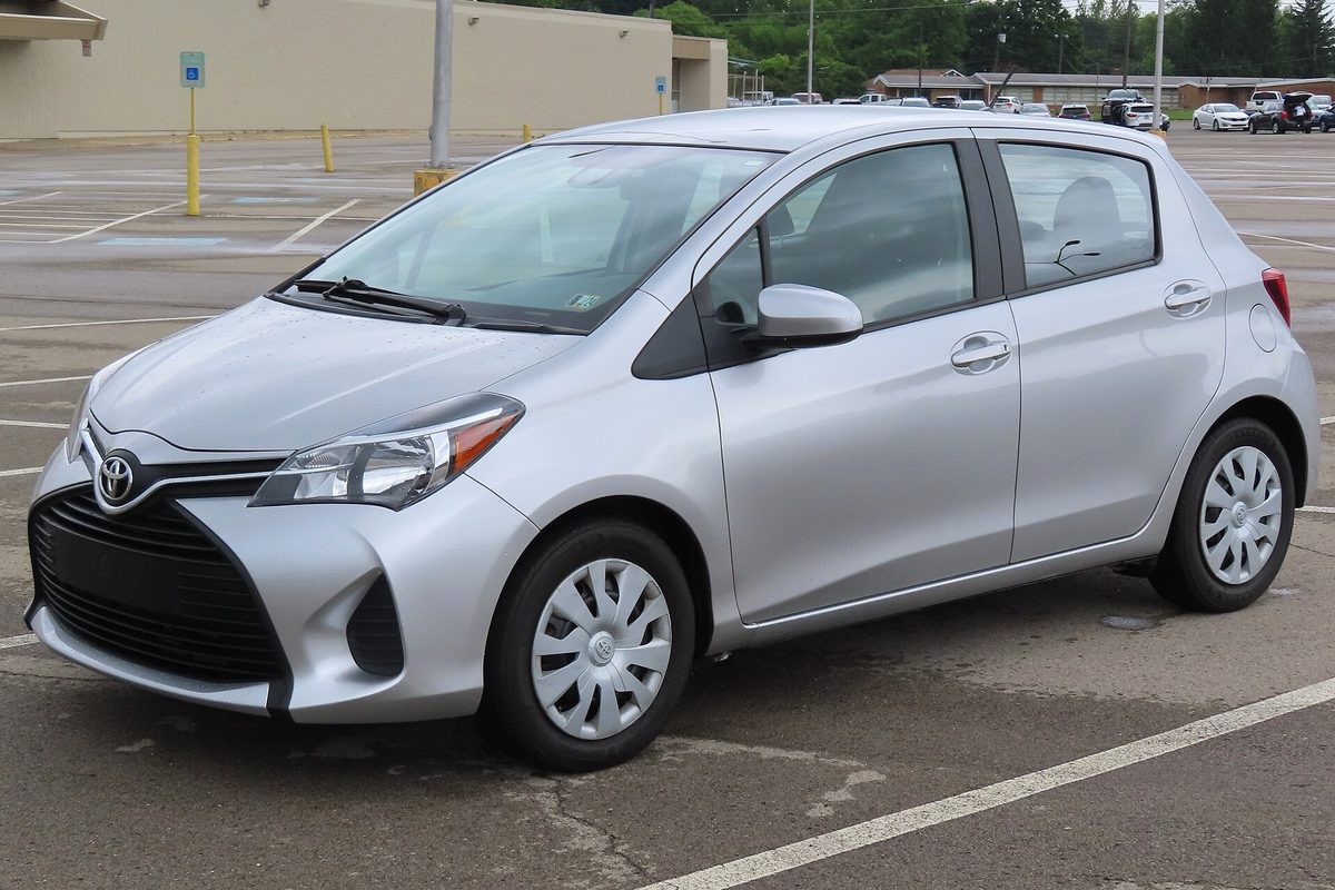 A silver 2017 Toyota Yaris L five-door hatchback with plastic wheel covers, parked alone in a wide, empty lot