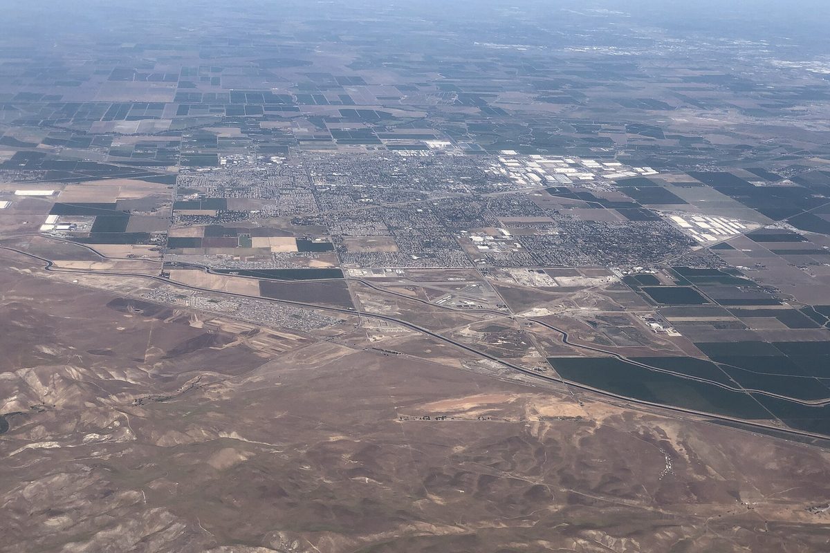 View from an airplane of Tracy spread across the flat valley floor, with bare brown hills and a freeway in the foreground and farm fields beyond