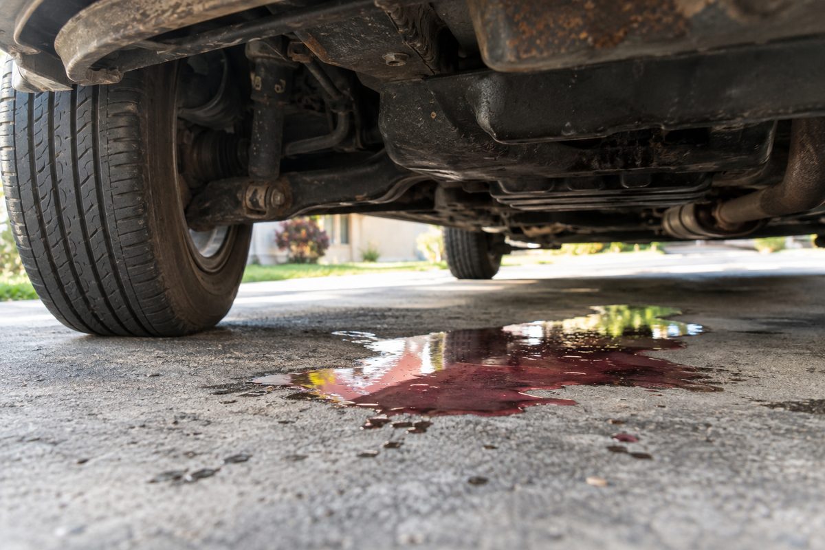 A reddish fluid puddle under the middle of a car on a driveway