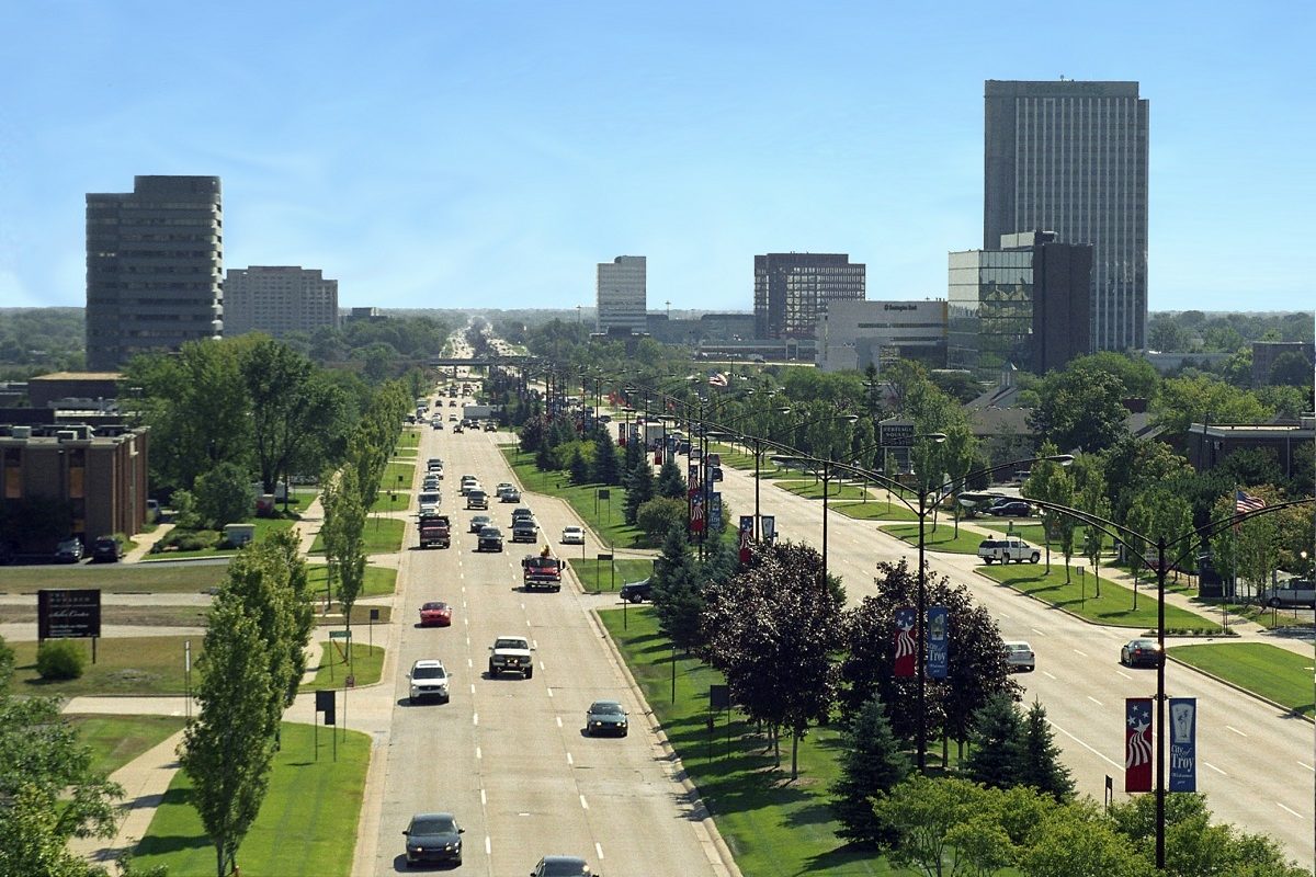 Big Beaver Road in Troy seen from above, a wide divided boulevard with traffic heading toward office towers on a clear summer day