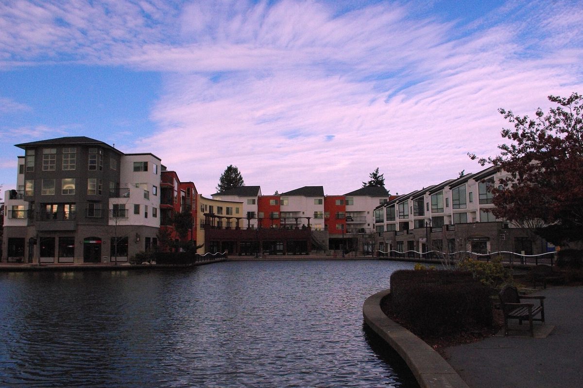 Colorful apartment and shop buildings around the lake at Tualatin Commons at dusk, with pink clouds overhead