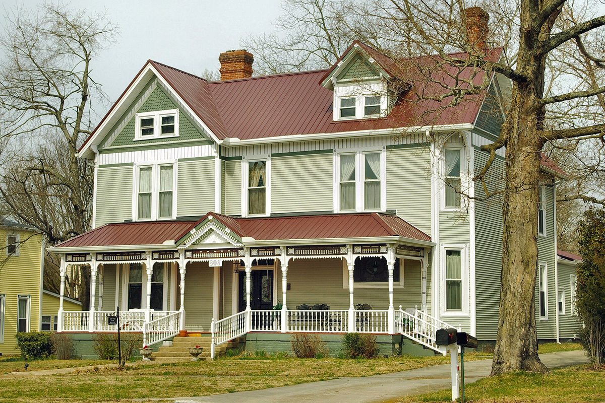 The Raht-Couch House in Tullahoma, a two-story Victorian home with pale green siding, a red metal roof and a white wraparound porch, behind bare trees