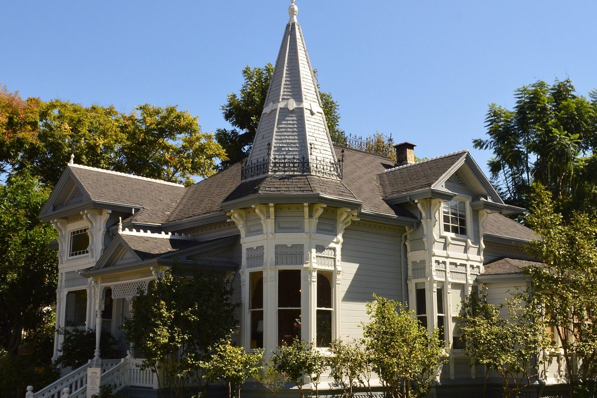 The gray Victorian Sherman Stevens House in Old Town Tustin, with a tall pointed turret, bay windows and trees under a clear blue sky