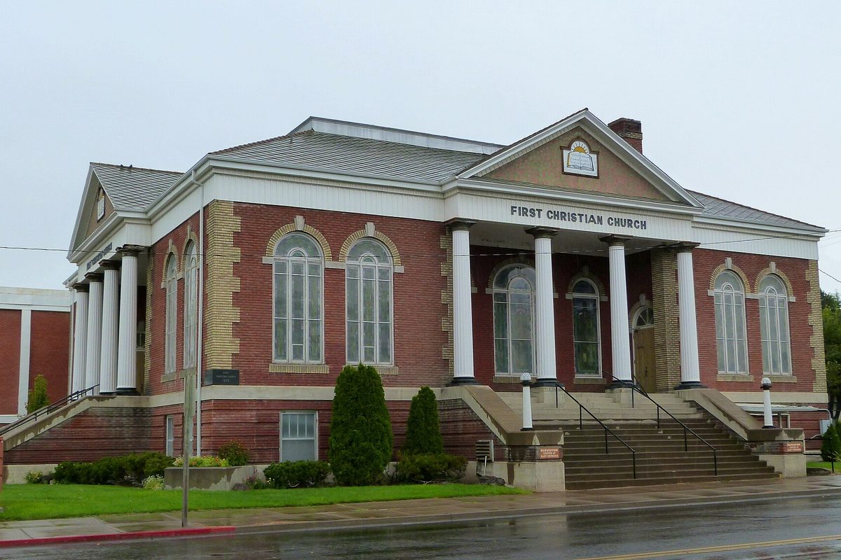 The red brick First Christian Church in Twin Falls, with white columns, arched windows and wide front steps, beside a wet street on a gray day