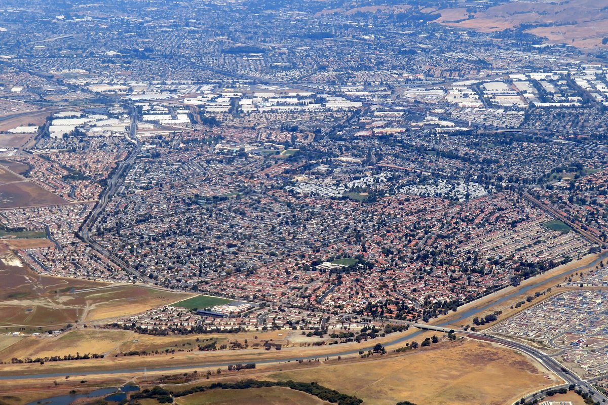 Aerial view of Union City's housing tracts and warehouse roofs, with a flood channel, a freeway and dry fields along the bottom edge