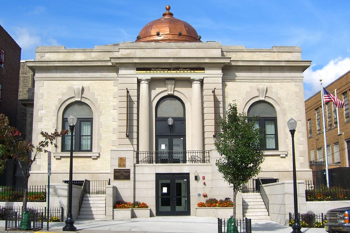 The William V. Musto Cultural Center in Union City, a pale stone building with a copper dome, three arched windows and an American flag beside it