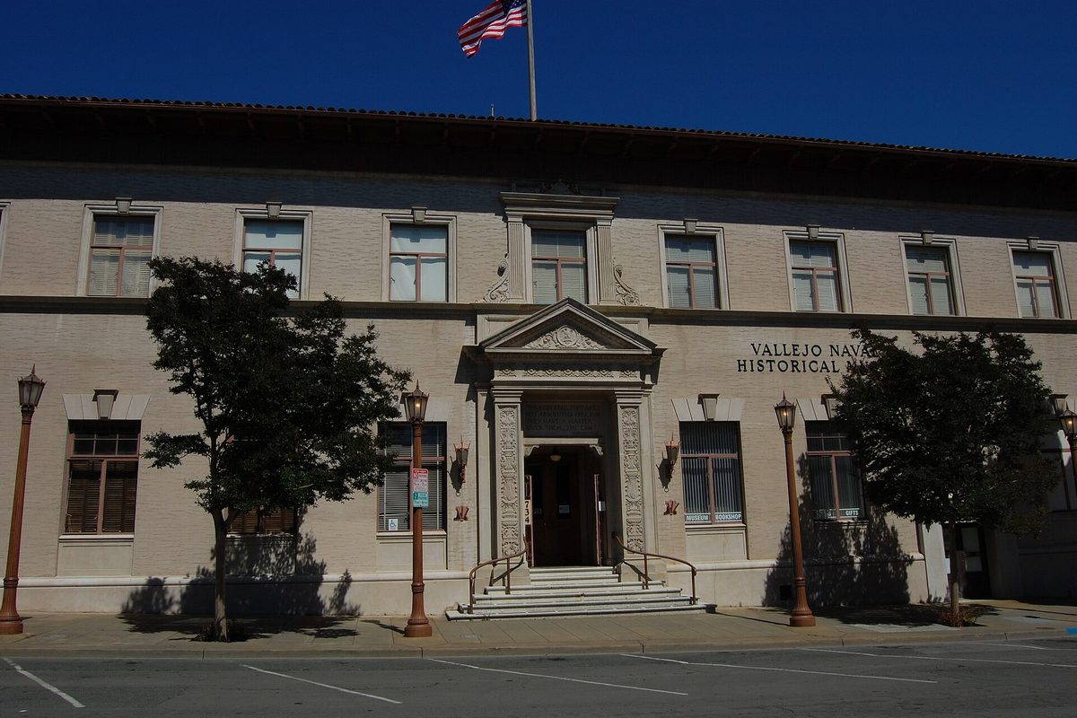 The pale stone Vallejo Naval and Historical Museum on Marin Street, the old City Hall, with a flag on the roof and lamp posts along the sidewalk