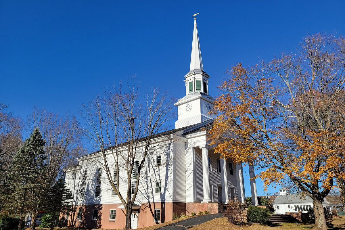 First Congregational Church in Vernon, white with tall columns and a clock steeple, beside an orange-leafed tree on a clear autumn day
