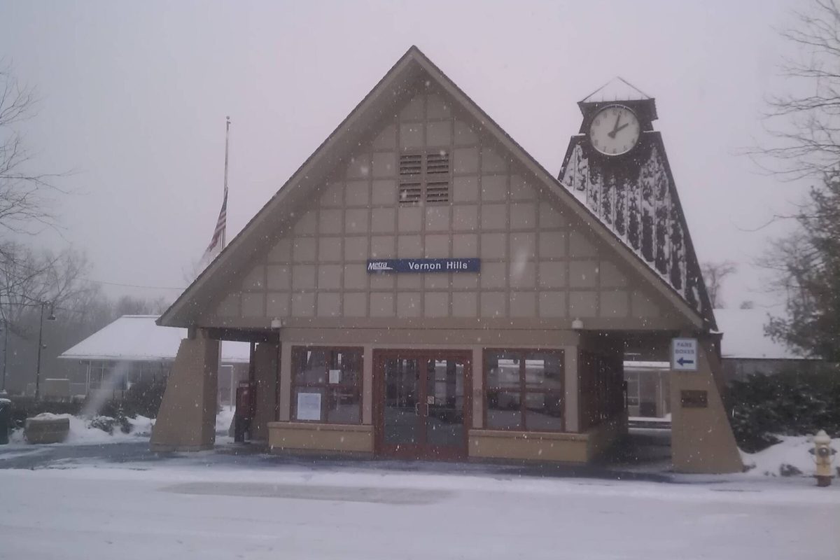 The Vernon Hills Metra station, a tan gabled building with a clock tower, during a heavy snowfall