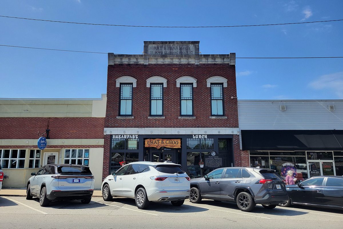 A two-story red brick storefront with arched upper windows and a breakfast and lunch cafe on the ground floor in downtown Villa Rica, with SUVs parked out front