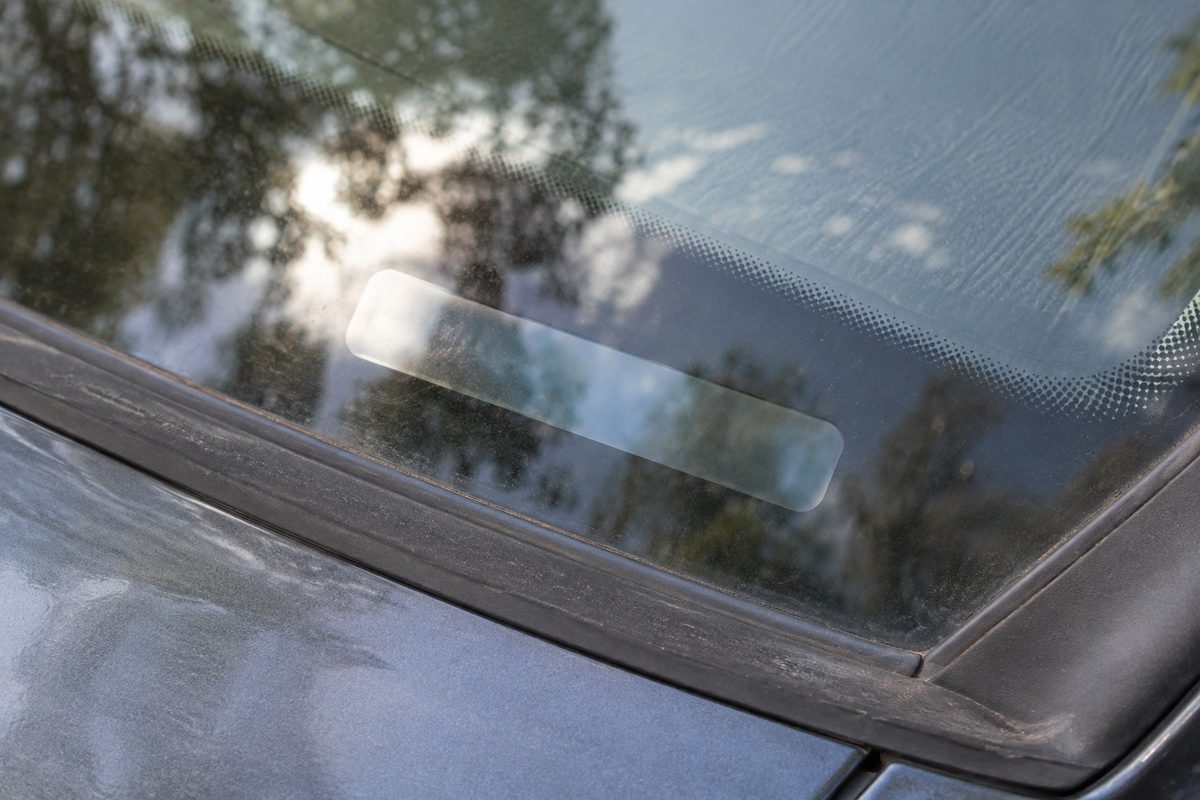 Close-up of a dusty windshield base with a blank clear plate where the VIN tag would sit, trees reflected in the glass