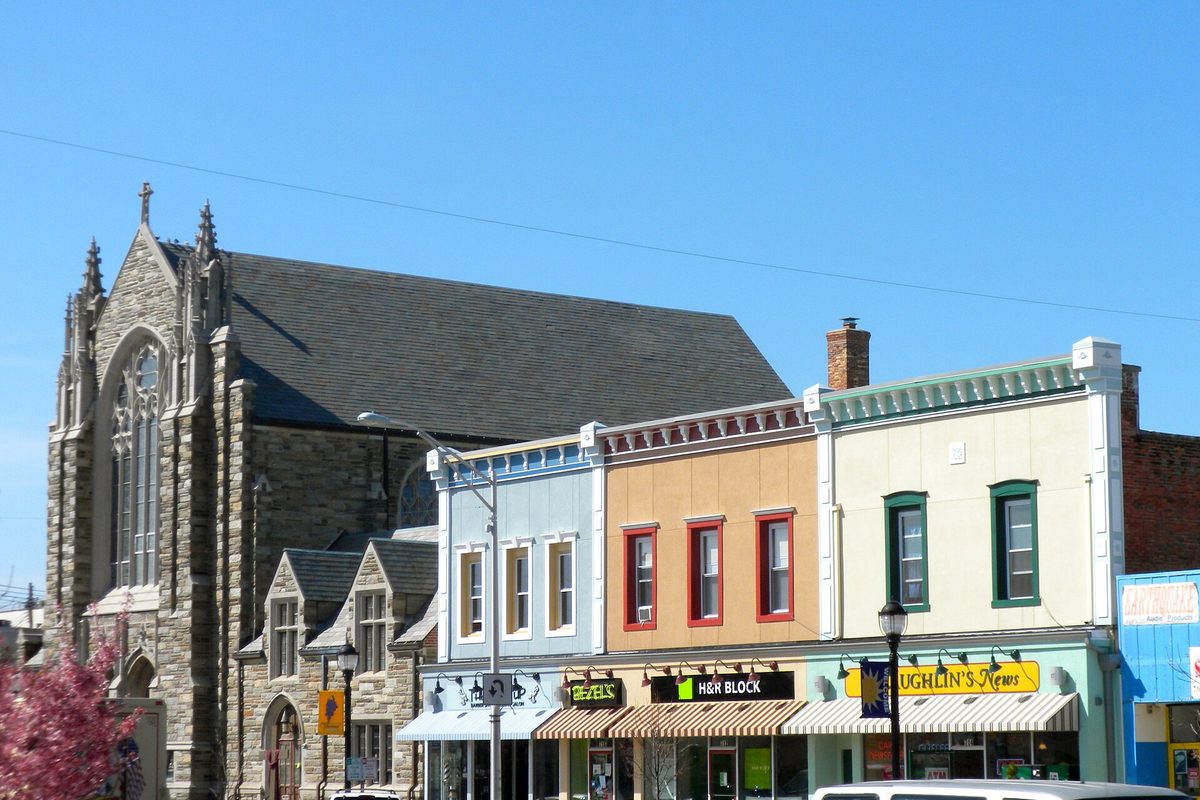 Colorful two-story storefronts with striped awnings beside a gray stone church on Landis Avenue in downtown Vineland, under a clear blue sky