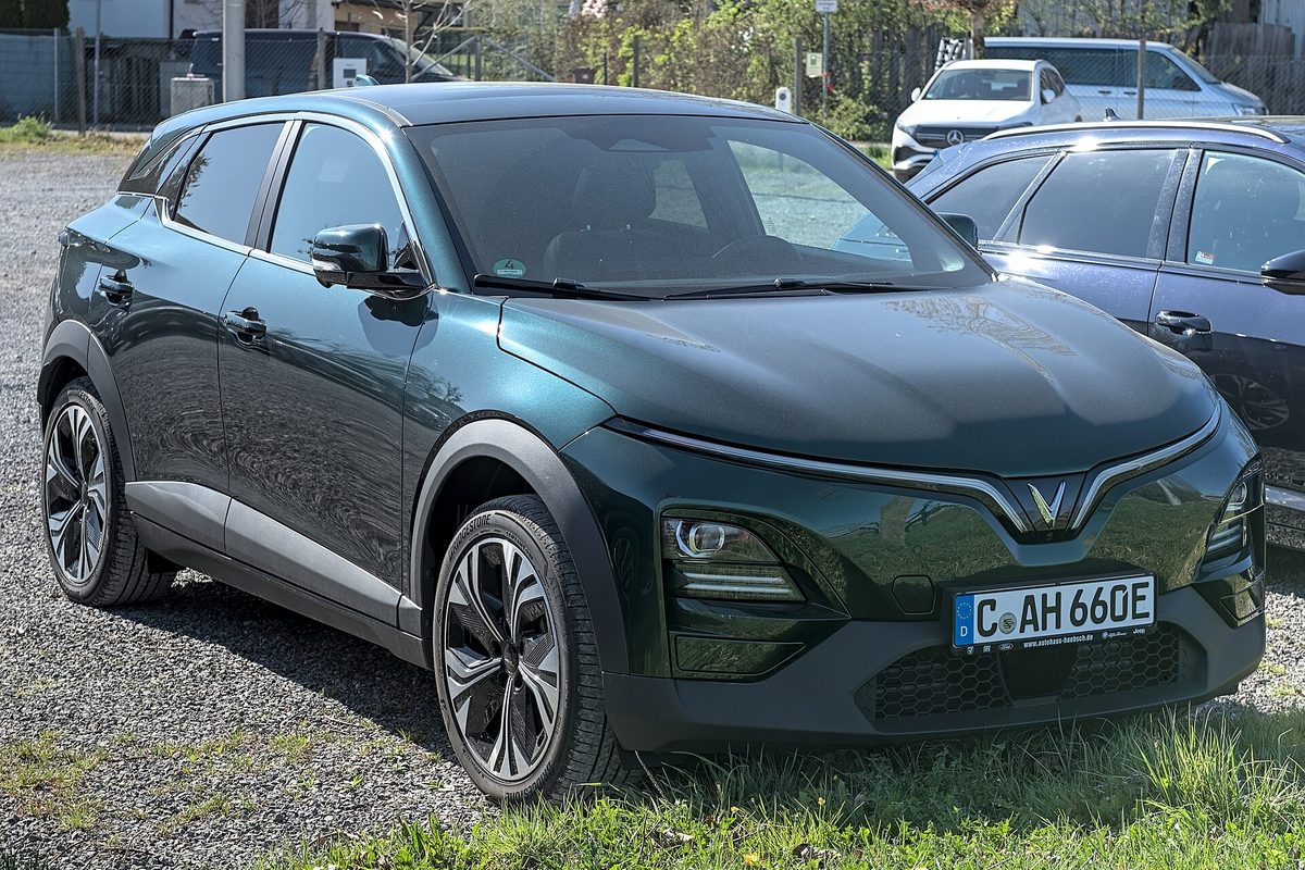 A dark green VinFast VF 6 small crossover parked on gravel beside other cars