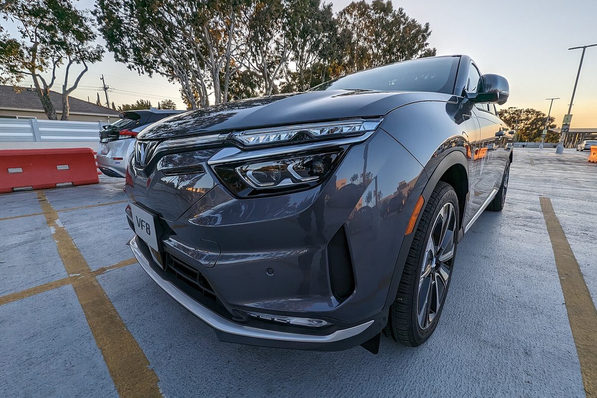 A gray VinFast VF 8 electric SUV seen low from the front corner, parked in an open parking lot at sunset
