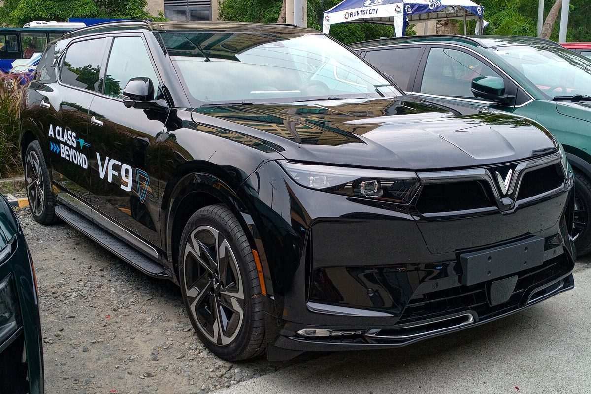 A black VinFast VF 9 SUV with VF9 lettering on the doors, parked on gravel next to other SUVs