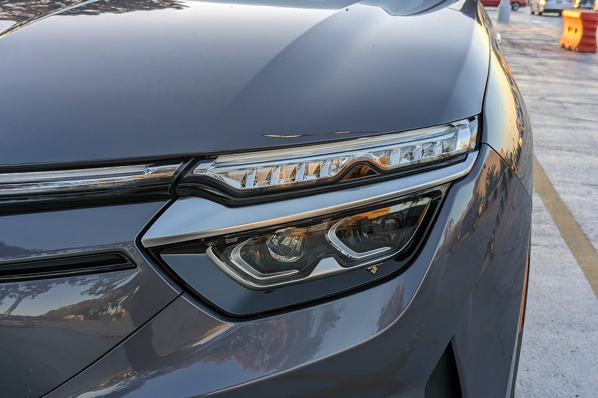 Close-up of the LED headlight and front fender of a gray VinFast VF 8 SUV parked at a shopping center in San Mateo, California