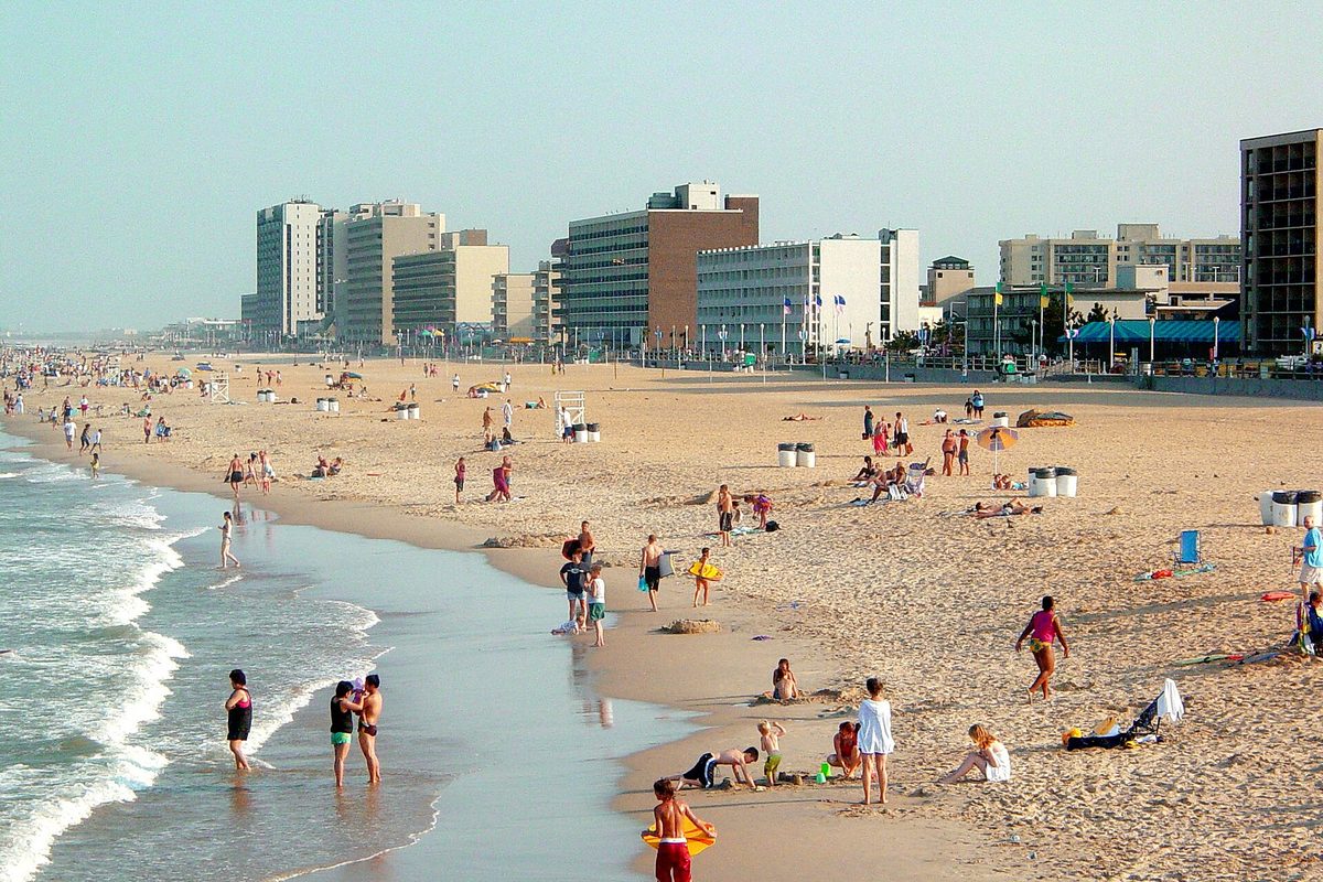 The Virginia Beach oceanfront seen from the fishing pier: swimmers in the surf, people on the sand, and a row of hotels along the boardwalk