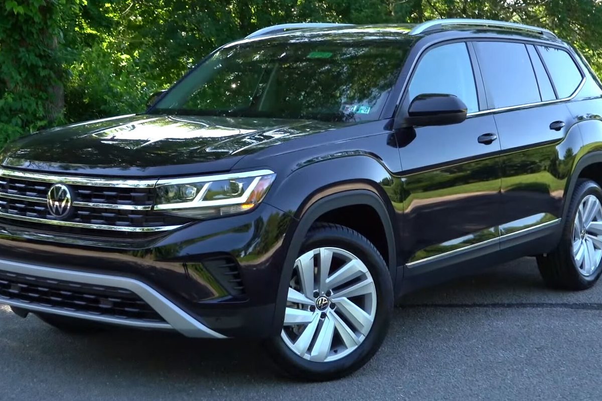 A dark purple-black 2021 Volkswagen Atlas SUV with silver alloy wheels, parked in front of green trees