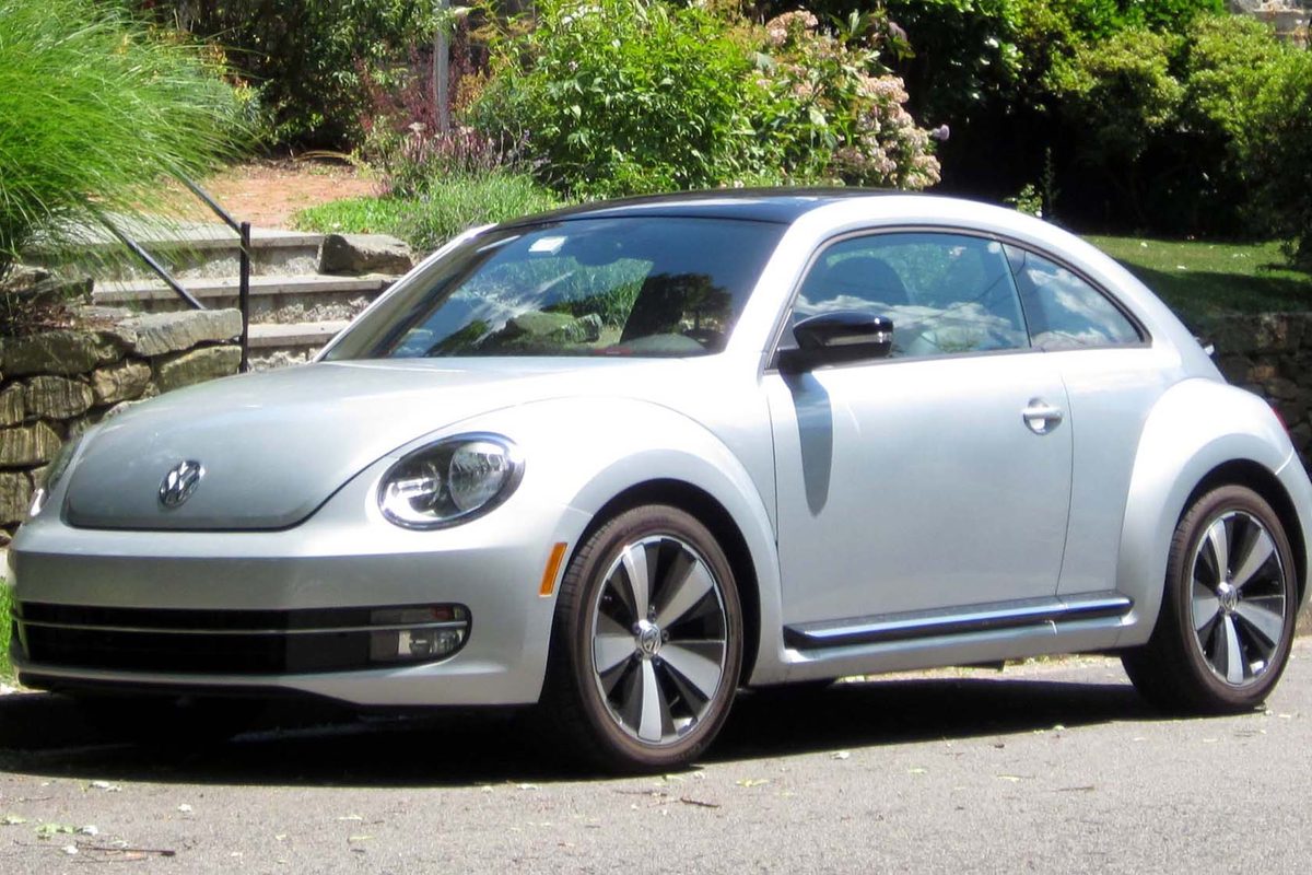A silver 2012 Volkswagen Beetle coupe parked on a street beside stone garden steps and shrubs