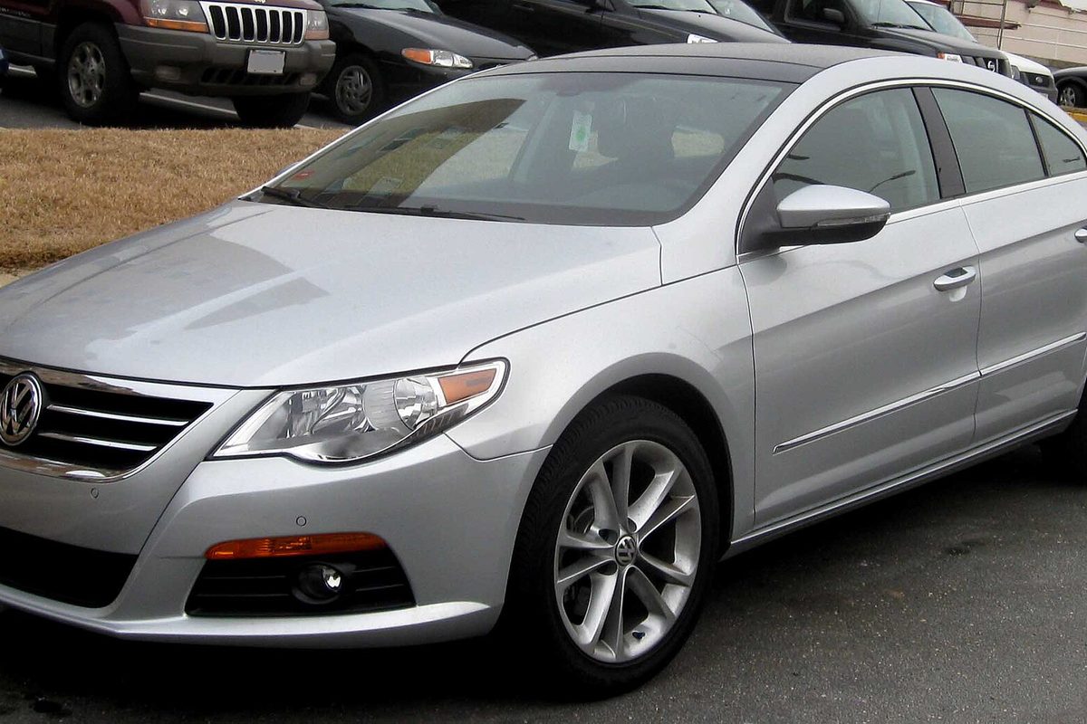 A silver Volkswagen CC four-door sedan parked in a lot next to other cars and a strip of dry grass