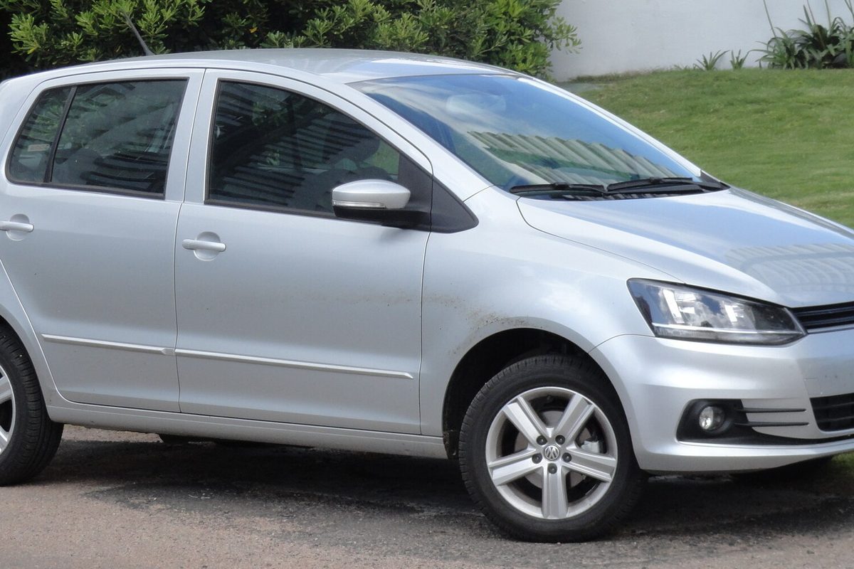 A silver Volkswagen Fox five-door hatchback, the later South American model, parked beside green hedges
